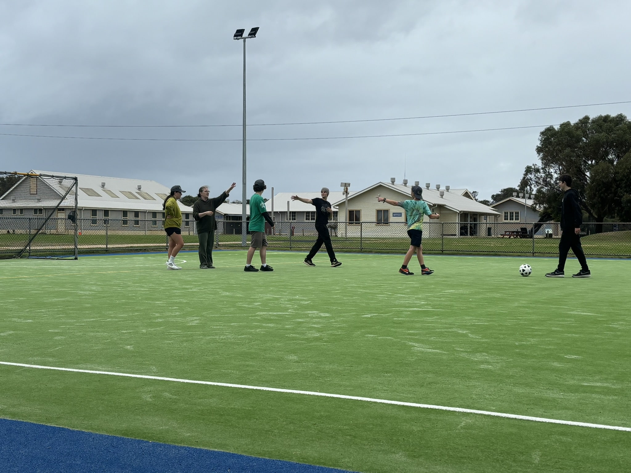 A group of six people is on an outdoor artificial turf sports field, engaging in a casual football game