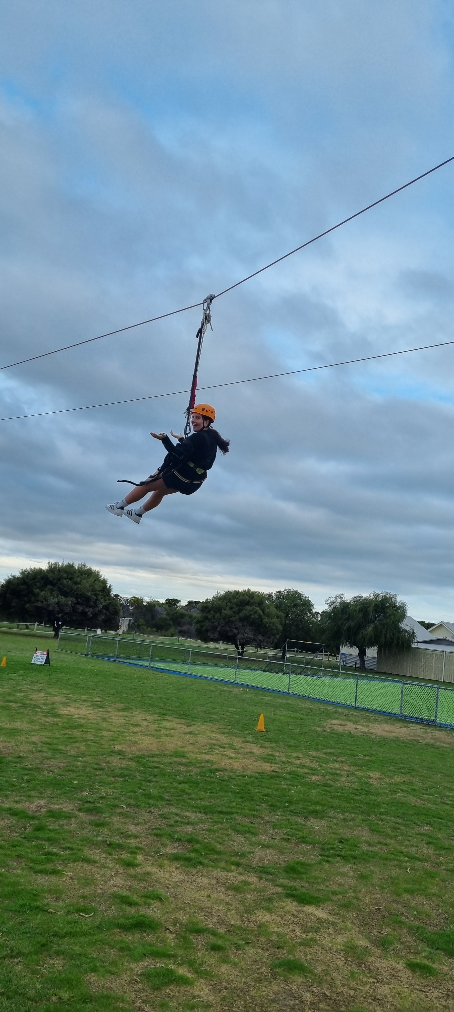 A child wearing a helmet and harness gliding on a zip line over a grass field